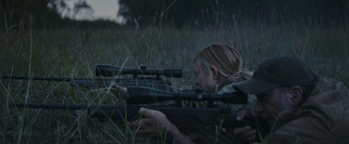 Zoe and her father sight down rifles as they hide in grass