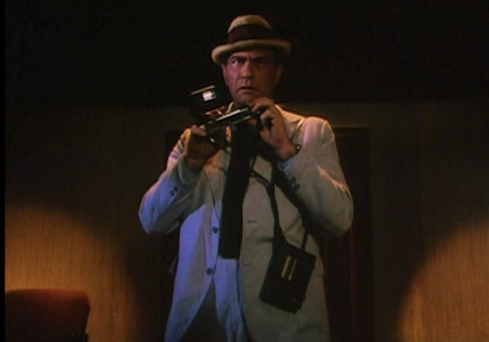 Carl Kolchak standing ready with his camera and tape recorder in trademark straw pork pie hat