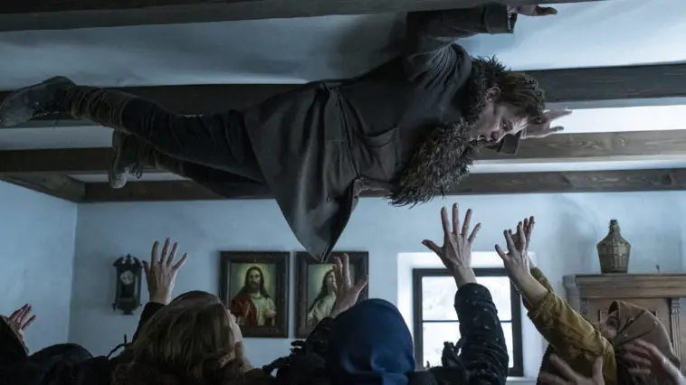 A man held on the ceiling by ghosts and a crowd under him