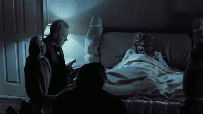 A possessed Reagan lies in bed while two priests read from the Bible
