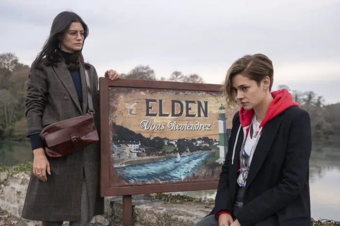 Emma and Camile sit in front of the Elden welcome sign, Emma being worried about how her welcome will be