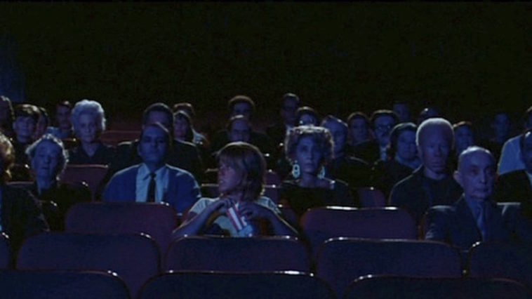 A theatre full of blank faced men and women stare at a movie screen