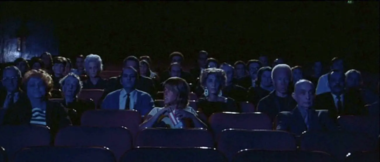 A theatre full of blank faced men and women stare at a movie screen