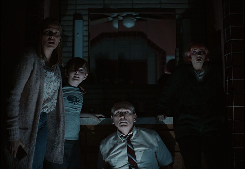 A family of four in a dark bathroom stare at the camera in terror.