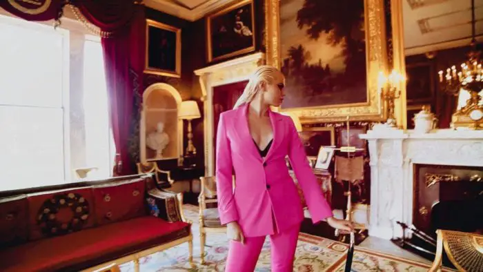 A young blonde woman in a pink suit stands in an extravagant living room