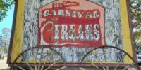 Weathered sign reminiscent of a carnival billboard announces "Carnival Freaks"