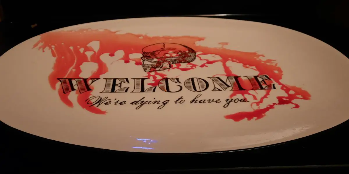 A serving tray reads "WELCOME, We're dying to have you" Blood runs down the surface of the tray.
