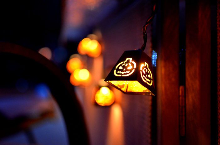 A metal bell hangs from a door with a glowing jack o'lantern engraved in it.