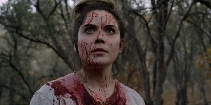 a woman covered in blood stares off screen