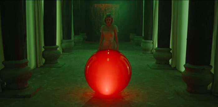 Margaret stands in a green room in front of a glowing red ball in The Blazing World