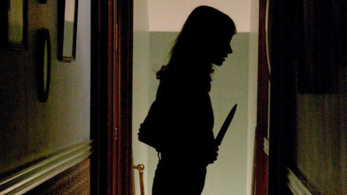 Samantha (Jocelin Donahue) stands silhouetted with a knife, searching for where the mysterious sounds are coming from