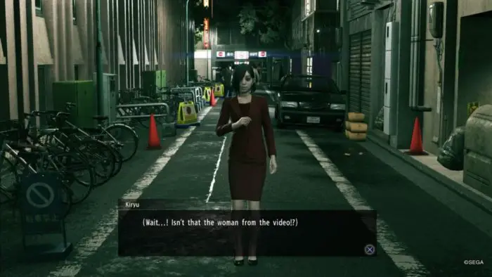 A disturbingly pale woman in red stands ominously in a street while Kiryu questions if she's the woman from a video he watched