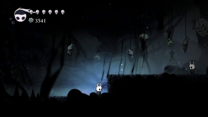 The player character in Hollow Knight approaches their doppelganger in the Deepnest. Various lifeless husks of other dwellers hang from the ceiling by mysterious threads.