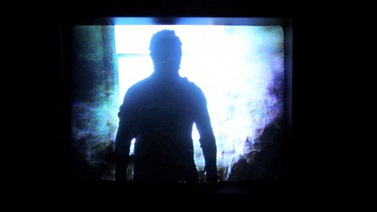 A man cast in shadow stands before a window, bathed in intense blue light