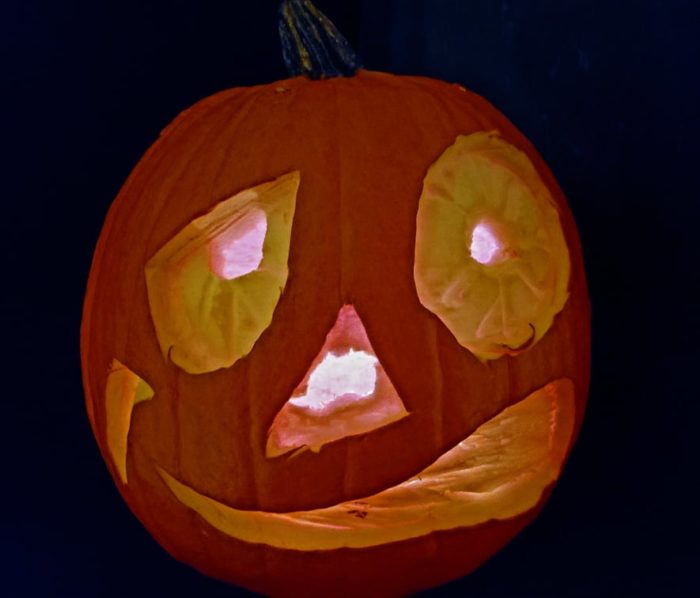 Bug-eyed, weird grinning pumpkin carved into a jack-o'-lantern, glowing in the dark.