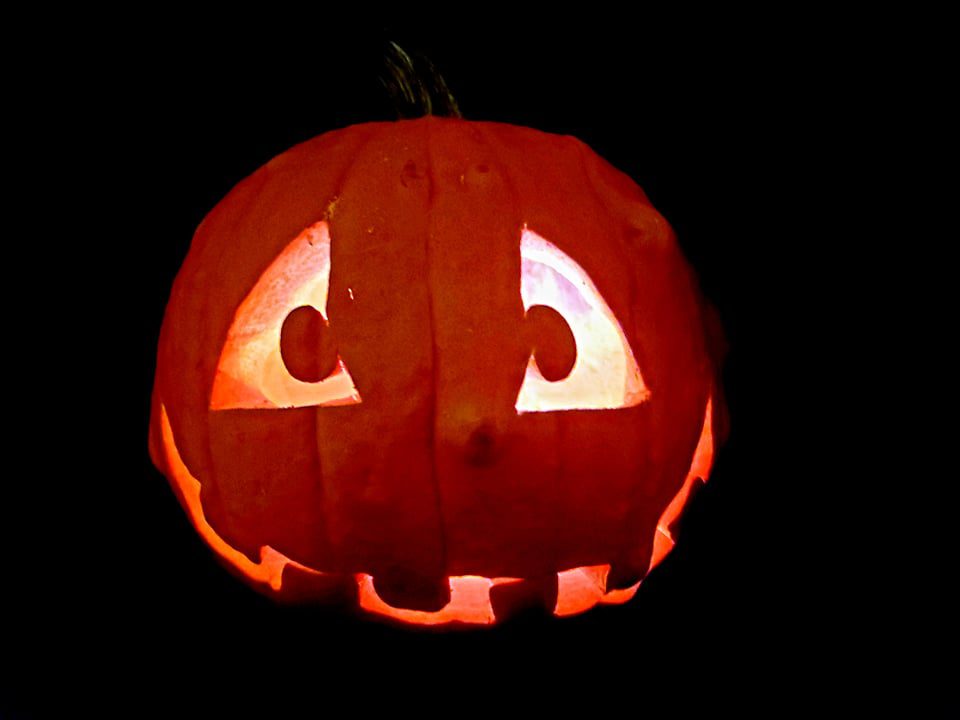 Carved pumpkin Jack-o'-lantern with a lit candle inside glowing in the dark, spreading a goofy grin.