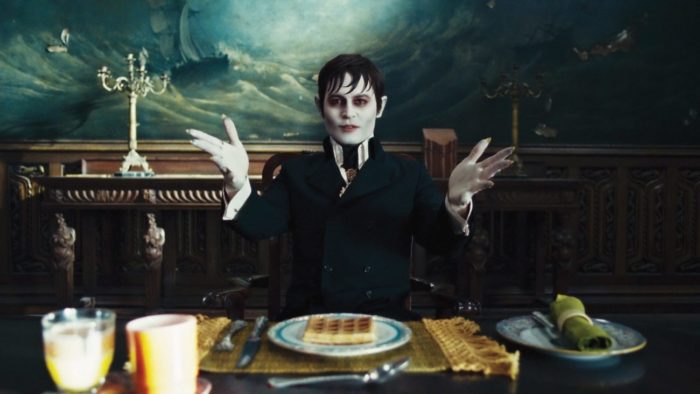 A pale vampire, played by Johnny Depp, sits at a table with his hands held open.