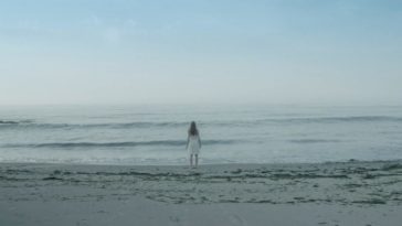 Charlie is at the water's edge on a beach in Alone With You