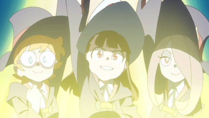 Three young girls dressed in uniform and witch hats with triumphant expressions, surrounded by a glowing yellow light.