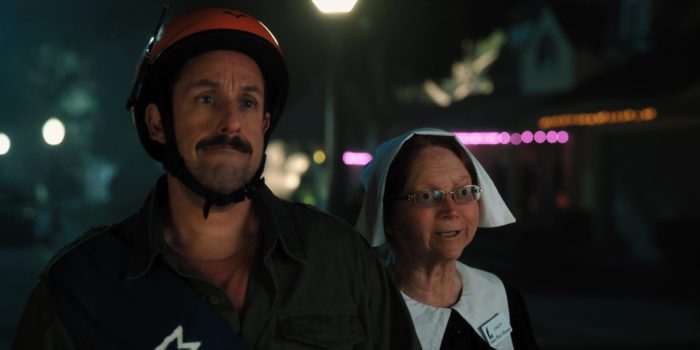 A man in a helmet, played by Adam Sandler, is stood next to a woman in a nurse costume.