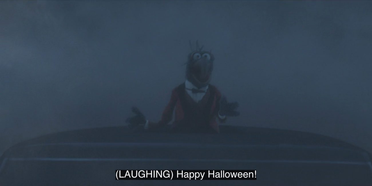 Gonzo laughs and yells, "Happy Halloween!" while standing in a sunroof on a hearse in a foggy night, in the 2021 special, "Muppets Haunted Mansion."
