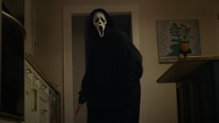 Ghostface stands in a kitchen doorway holding a bloody knife in Scream (2022)