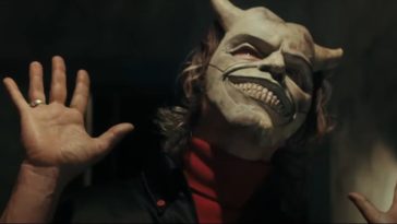 Ethan Hawke holds his hands up while donning a smiling devil mask in The Black Phone