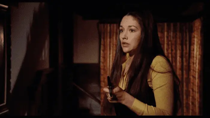 Olivia Hussey as Jess in Black Christmas wields a weapon while looking frightened