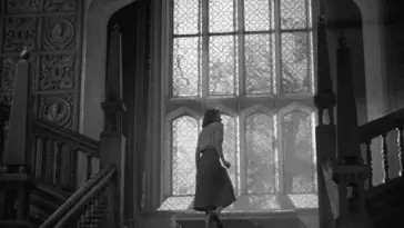 Screenshot of Rebecca shows a woman ascending a grand staircase near a large ornate window