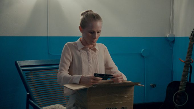 a woman in a stiff work uniform sits in a warehouse corner in stanleyville