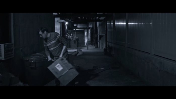 The Man takes out the trash, as a specter spectates from behind him