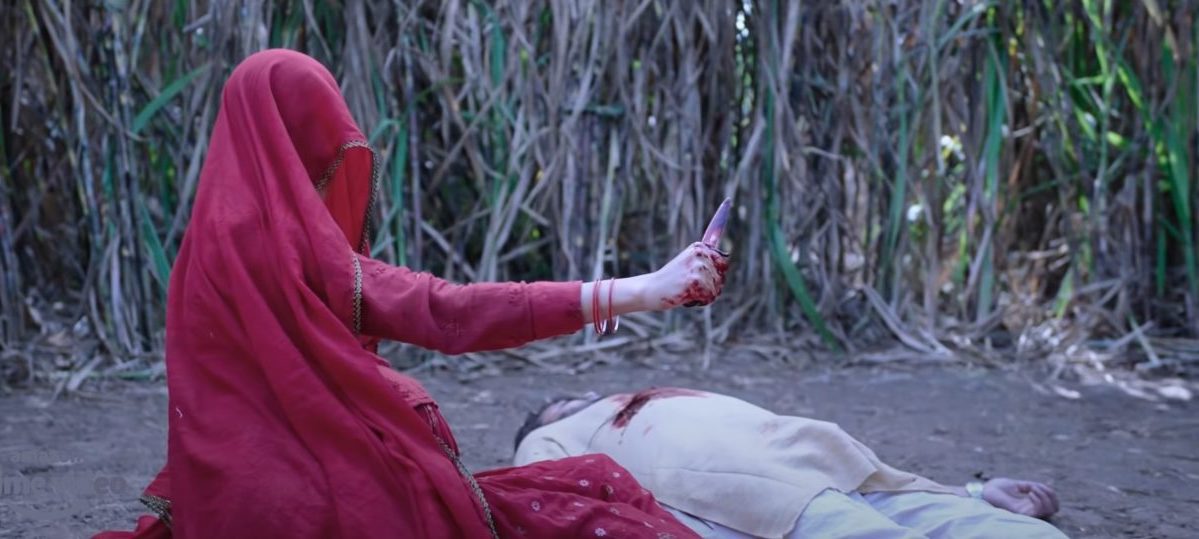 A woman wearing all red lifts a dagger above a bloody body in a sugarcane field in Chhorii.