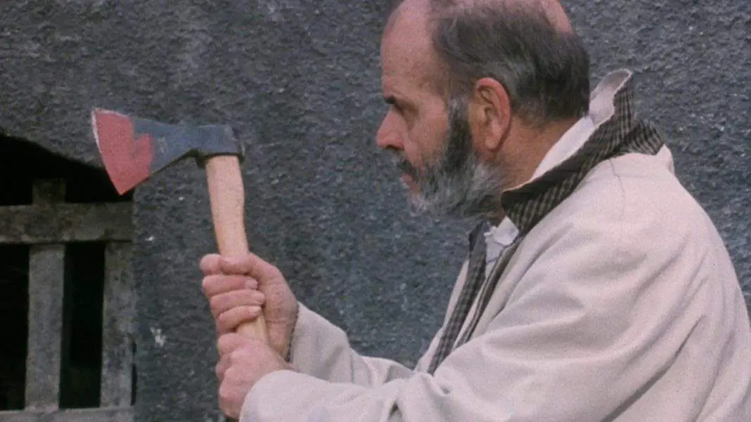 Seen in profile, a man with thinning, graying hair and a graying beard holds up in front of him, with both hands on the handle, a short axe.