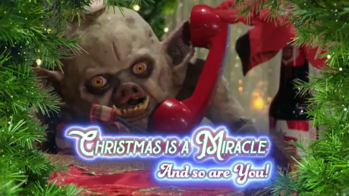 the puppet of a gremlin-like creature talks on the phone at a christmas themed table. the phrase "Christmas is a miracle, and so are you!" is displayed
