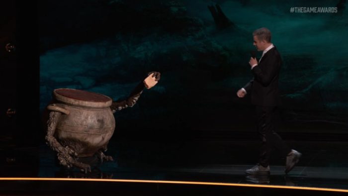 A large puppet of an ornate pot with arms hands Geoff an envelope on the stage of The Game Awards