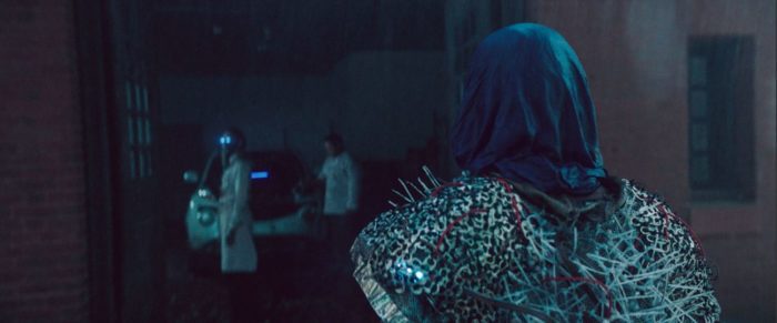 Moretz enters a hostile android filled garage while one of the robots casts its blue gaze in her direction in Mother/Android