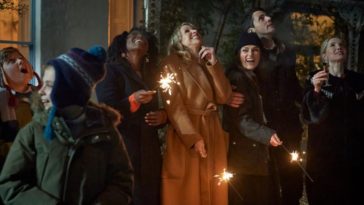 The cast of Silent Night stand outside in heavy winter coats lighting sparklers and looking at the sky.