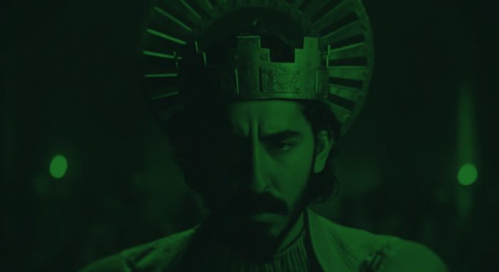 A man wearing a crown cast in green light looks pensive in Green Knight