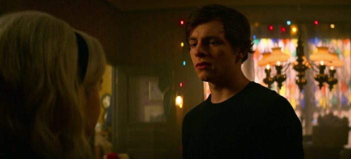 Harvey looks uncomfortable as he speaks to Sabrina with Christmas lights in the background.