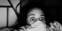 A person lying in bed pulls a sheet up over their face leaving exposed wide open eyes.