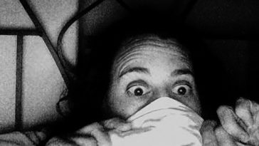 A person lying in bed pulls a sheet up over their face leaving exposed wide open eyes.