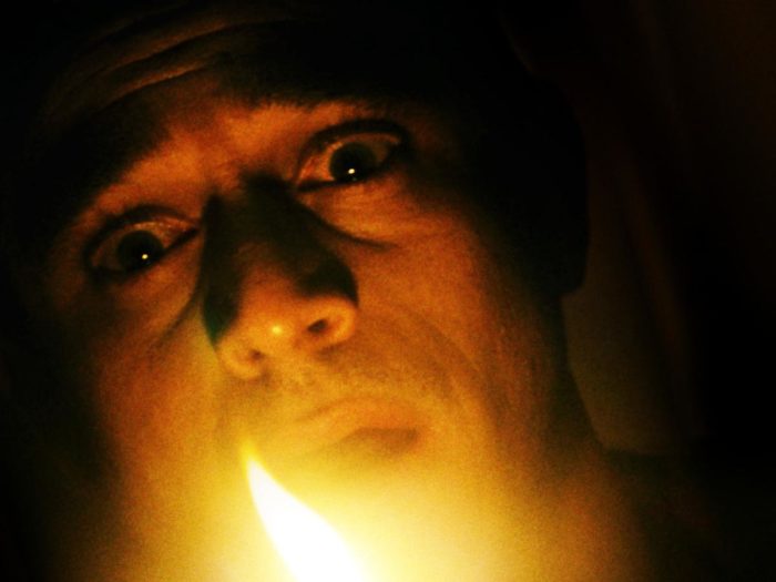 Close frame of a man looking fearful lit by candle flame in The Vigil