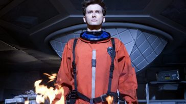 The Tenth Doctor, wearing an orange spacesuit and standing in front of a fire