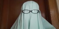 A "ghost" wearing a sheet and reading glasses stands in a doorway