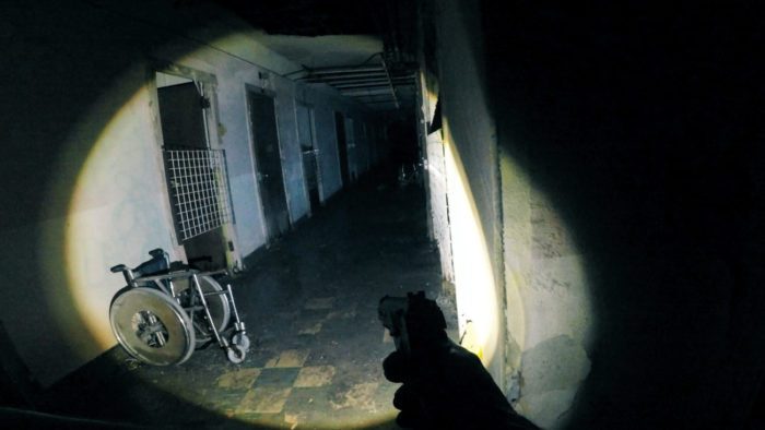 A first-person perspective on a dark hallway lit by a flashlight