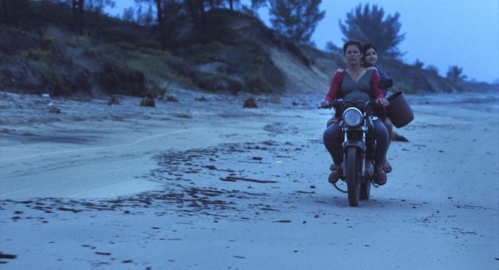 two people rides a motorbike on a beach