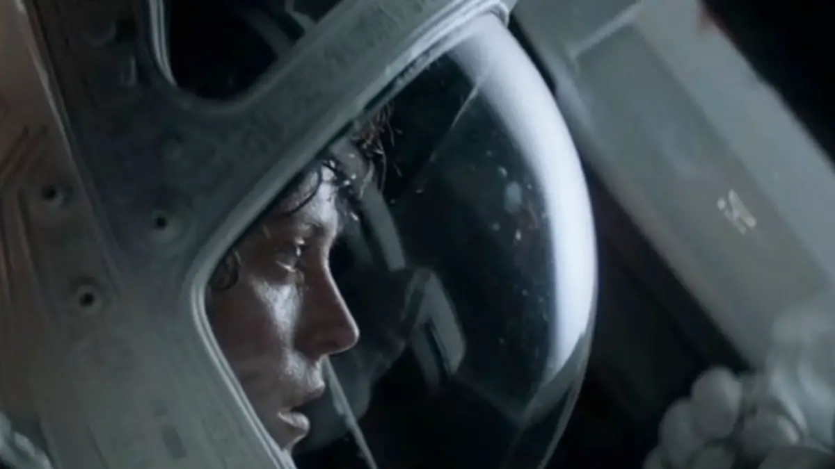 A woman in profile looks into the distance out of a round astronaut's helmet.