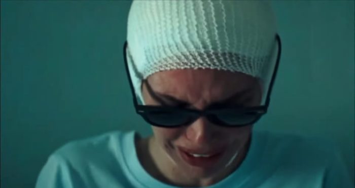 Diana cries sitting in her hospital gown, wearing bandages on her head and Dark Glasses