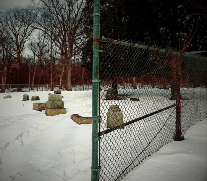 An opening in the fence revealing tombstones and trees in Bachelor's Grove