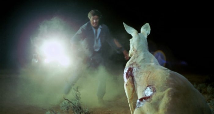 A man stands before a bloodied kangaroo, seemingly ready to attack or be attacked.
